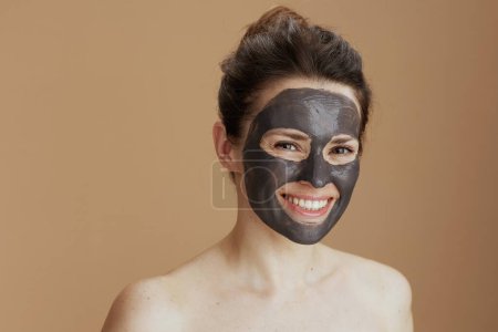 Téléchargez les photos : Femme moderne souriante avec masque cosmétique sur fond beige. - en image libre de droit