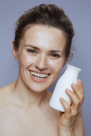 Téléchargez les photos : Portrait de souriante femme d'âge moyen moderne avec pot de crème cosmétique sur fond bleu. - en image libre de droit