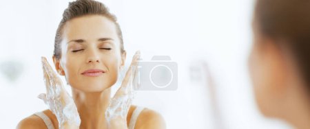 Téléchargez les photos : Jeune femme lavage visage dans la salle de bain - en image libre de droit