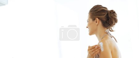 Téléchargez les photos : Jeune femme appliquant la crème sur l'épaule dans la salle de bain - en image libre de droit
