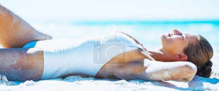 Happy young woman in swimsuit tanning on beach