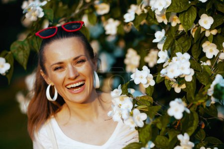 Photo for Summer time. Portrait of happy elegant female in white shirt near flowering tree. - Royalty Free Image