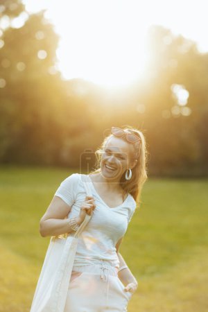 Foto de Hora de verano. feliz joven hembra en camisa blanca con bolso de mano en el prado en el parque de la ciudad. - Imagen libre de derechos