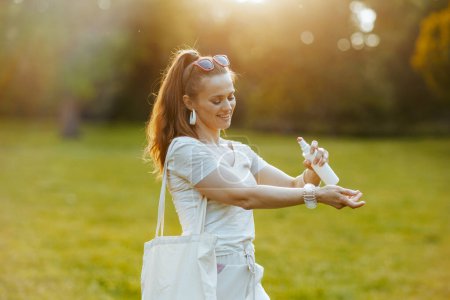 Summer time. happy trendy woman in white shirt with tote bag using spf in the meadow outside in nature.
