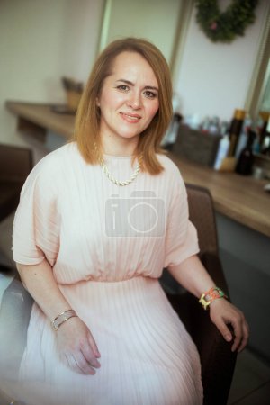 Photo for Portrait of smiling woman hair salon client in pink dress in modern hair studio sitting in chair. - Royalty Free Image