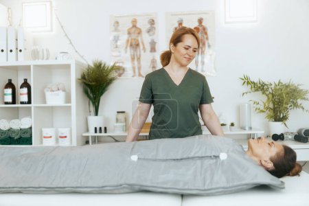 Tiempo de atención médica. terapeuta de masaje médico femenino sonriente en gabinete de masaje con cliente haciendo procedimiento de envoltura de whisky en manta térmica.