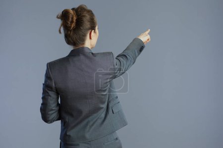 Foto de Visto desde atrás trabajadora de mediana edad en traje gris apuntando a algo aislado sobre fondo gris. - Imagen libre de derechos
