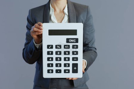 Photo for Closeup on woman worker in grey suit with calculator against gray background. - Royalty Free Image