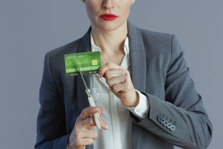 Téléchargez les photos : Gros plan sur une employée en costume gris avec carte de crédit et ciseaux sur fond gris. - en image libre de droit