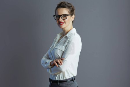 Téléchargez les photos : Heureux à la mode 40 ans femme employée en chemisier blanc avec des lunettes sur fond gris. - en image libre de droit