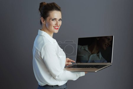 Photo for Smiling stylish middle aged business woman in white blouse using laptop isolated on grey. - Royalty Free Image