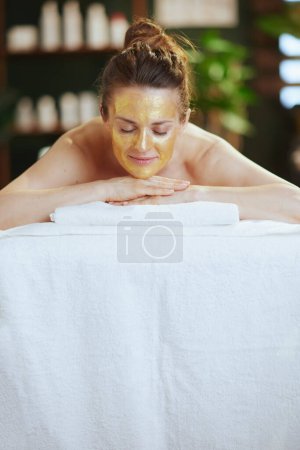 Temps de santé. femme moderne détendue de 40 ans dans un salon de spa avec masque cosmétique doré sur le visage posé sur une table de massage.
