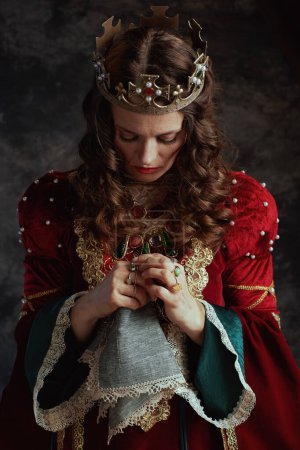Photo for Sad medieval queen in red dress with handkerchief and crown on dark gray background. - Royalty Free Image