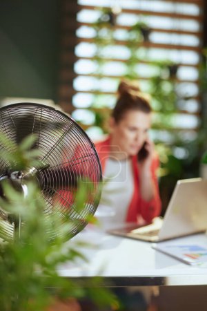 Photo for Sustainable workplace. Closeup on smiling modern accountant woman at work with electric fan and laptop. - Royalty Free Image