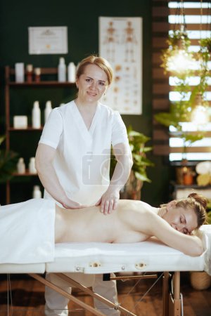 Foto de Tiempo de atención médica. terapeuta de masaje médico sonriente en el gabinete de masaje hacer una terapia de masaje en la mesa de masaje. - Imagen libre de derechos