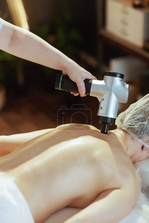 Foto de Tiempo de atención médica. Primer plano del terapeuta de masaje médico en el gabinete de masaje con pistola de masaje que masajea el cuello de los clientes. - Imagen libre de derechos