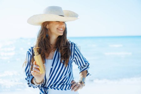 Téléchargez les photos : Femme élégante souriante sur la plage avec écran solaire. - en image libre de droit