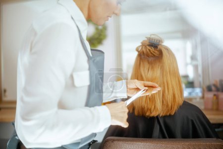 Closeup on woman hairdresser in modern hair studio with scissors and client cutting hair.