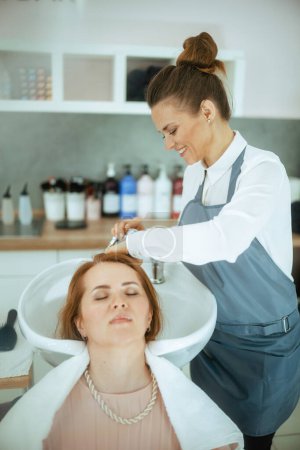 Téléchargez les photos : Coiffeuse dans un studio de beauté moderne avec client détendu laver les cheveux. - en image libre de droit