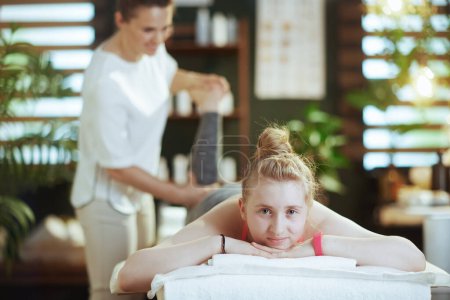 Photo for Healthcare time. female massage therapist in massage cabinet with teenage client making massage on massage table. - Royalty Free Image
