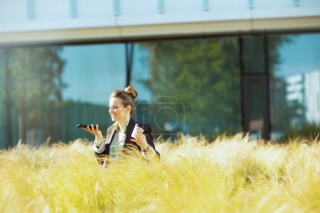 Photo for Happy modern female employee near business center in black jacket with smartphone and cup of coffee. - Royalty Free Image