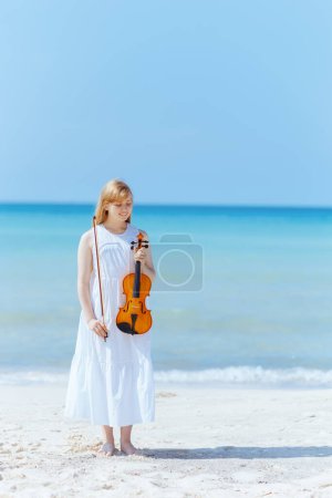 Photo for Full length portrait of smiling modern young woman in white dress on the seacoast with violin. - Royalty Free Image