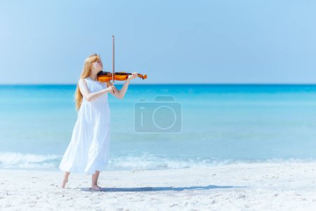 Photo for Full length portrait of modern young woman in light dress with violin enjoying playing on the seacoast. - Royalty Free Image