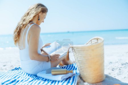 relaxed elegant female on the ocean coast with straw bag, book and striped towel.
