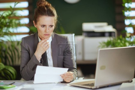Un nuevo trabajo. mujer moderna de mediana edad empleado en la oficina verde moderna en traje de negocios gris con ordenador portátil.
