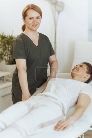 Téléchargez les photos : Temps de santé. souriant massothérapeute féminine dans l'armoire de massage avec le client faisant check-up. - en image libre de droit