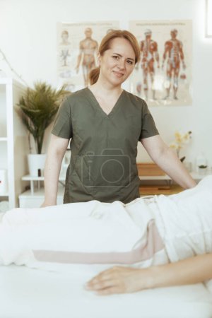 Téléchargez les photos : Temps de santé. souriant massothérapeute femme dans l'armoire de massage avec client conduisant l'examen. - en image libre de droit
