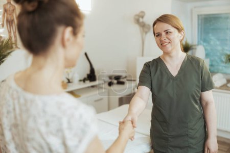 Téléchargez les photos : Temps de santé. Massothérapeute féminine souriante dans une armoire de massage avec client serrant la main. - en image libre de droit