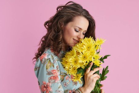 Foto de Mujer elegante y relajada en vestido floral con flores de crisantemos amarillos aisladas sobre fondo rosa. - Imagen libre de derechos