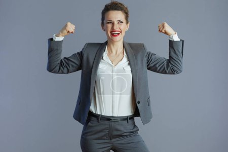 Photo for Happy 40 years old small business owner woman in gray suit showing biceps against gray background. - Royalty Free Image