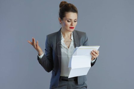 elegante 40-jährige Geschäftsfrau im grauen Anzug mit Dokument auf grauem Hintergrund.
