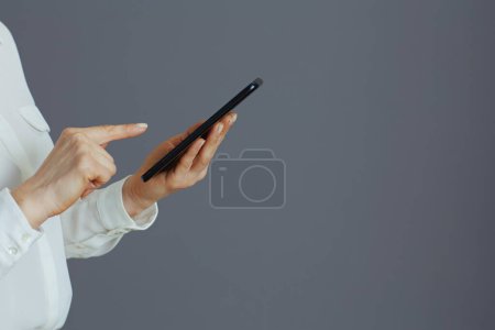 Téléchargez les photos : Gros plan sur une employée en chemisier blanc à l'aide d'applications smartphone isolées sur fond gris. - en image libre de droit