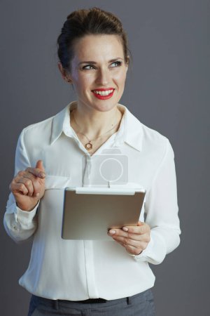 Téléchargez les photos : Coûteux travailleur femme à la mode en chemisier blanc en utilisant la tablette PC isolé sur fond gris. - en image libre de droit