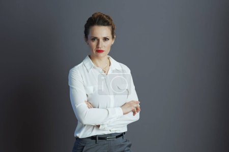 stylische Kleinunternehmerin in weißer Bluse vor grauem Hintergrund.