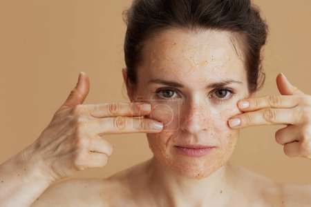 Téléchargez les photos : Femme d'âge moyen avec gommage du visage sur fond beige. - en image libre de droit