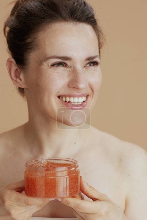 Foto de Mujer joven feliz con exfoliante facial sobre fondo beige. - Imagen libre de derechos