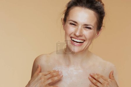 Photo for Smiling modern female rubbing body cream isolated on beige background. - Royalty Free Image