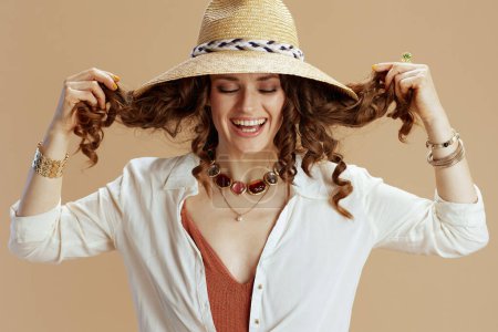 Foto de Vacaciones en playa. mujer moderna sonriente en blusa blanca y pantalones cortos aislados sobre fondo beige con sombrero de paja. - Imagen libre de derechos