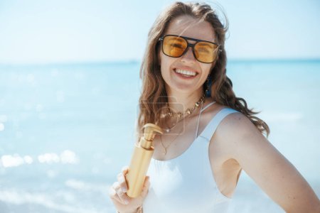smiling modern female on the ocean coast with sunscreen.