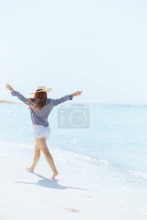 Photo for Full length portrait of smiling elegant 40 years old woman on the seacoast with straw hat rejoicing. - Royalty Free Image