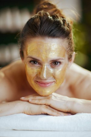 Temps de santé. femme moderne détendue dans une armoire de massage avec masque cosmétique doré sur la pose du visage sur la table de massage.