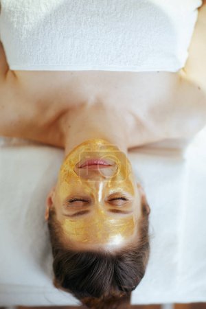 Photo for Healthcare time. Upper view of relaxed modern woman in massage cabinet with golden cosmetic mask on face laying on massage table. - Royalty Free Image