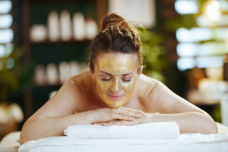Photo for Healthcare time. relaxed modern 40 years old woman in spa salon with golden cosmetic mask on face laying on massage table. - Royalty Free Image