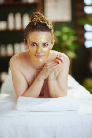 Foto de Tiempo de atención médica. relajado femenino moderno en el gabinete de masaje con máscara cosmética dorada en la cara que pone en la mesa de masaje. - Imagen libre de derechos