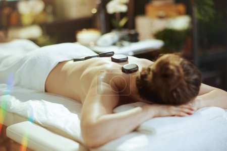 Téléchargez les photos : Temps de santé. moderne détendue 40 ans femme dans le salon de spa ayant massage aux pierres chaudes et la pose sur la table de massage. - en image libre de droit