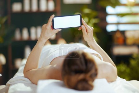 Photo for Healthcare time. relaxed modern female in spa salon with blank screen mobile phone laying on massage table. - Royalty Free Image